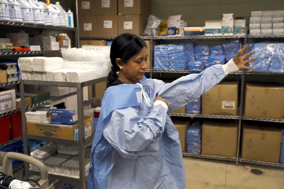 In this Tuesday, May 5, 2020, photo, Cook County Chief Medical Examiner Dr. Ponni Arunkumar, puts on personal protective equipment as she prepares to perform four autopsies in as many hours at the county morgue in Chicago. Arunkumar starts her day with a numbers problem. It's how to manage a tripling of death cases with the same number of pathologists and the same number of hours in a day as before COVID-19. (AP Photo/Charles Rex Arbogast)