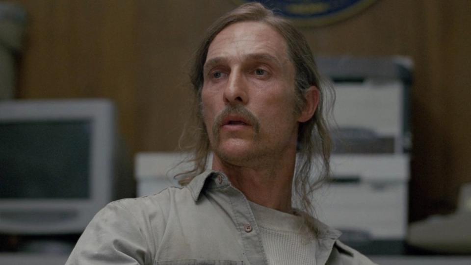 Matthew McConaughey's Rust Cohle with long hair and a mustache sitting down in True Detective Season One