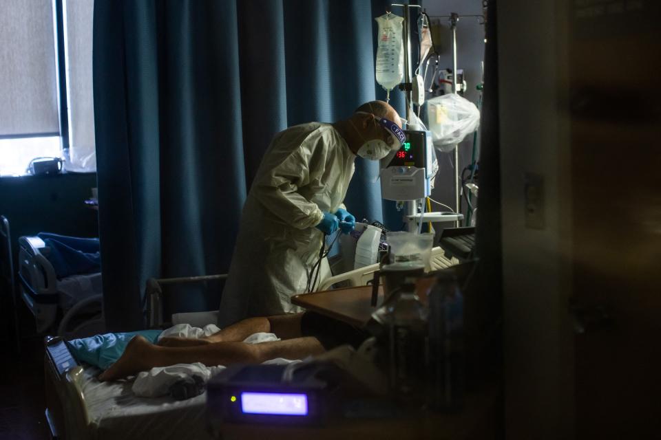 A doctor wearing protective gear checks on a COVID-19 patient lying in a hospital bed. 