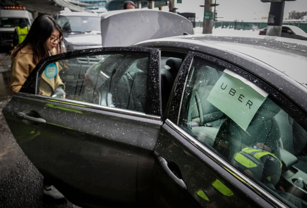 A person entering a vehicle with "Uber" written on a piece of paper on the right passenger window."