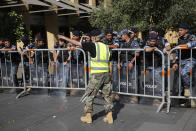 A retired Lebanese retired soldier, in yellow vest, protests in front of riot police who blocked a road leading to the parliament building where lawmakers and ministers are discussing the draft 2019 state budget, in Beirut, Lebanon, Tuesday, July 16, 2019. The lawmakers have begun discussing the budget amid tight security and limited protests against proposed austerity measures. The proposed budget aims to avert a financial crisis by raising taxes and cutting public spending in an effort to reduce a ballooning deficit. (AP Photo/Hussein Malla)