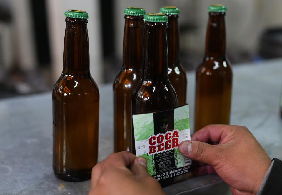 Un trabajador coloca el rótulo sobre botellas de cerveza hechas con hoja de coca en la licorería El Viejo Roble en La Paz, Bolivia, el viernes 3 de mayo de 2024. La Coca Beer es la nueva apuesta de una destilería boliviana que busca recuperar esta ancestral planta considerada sagrada por antiguos pueblos andinos y que es mal vista por el mundo por ser materia prima de la cocaína. (AP Foto/Juan Karita)