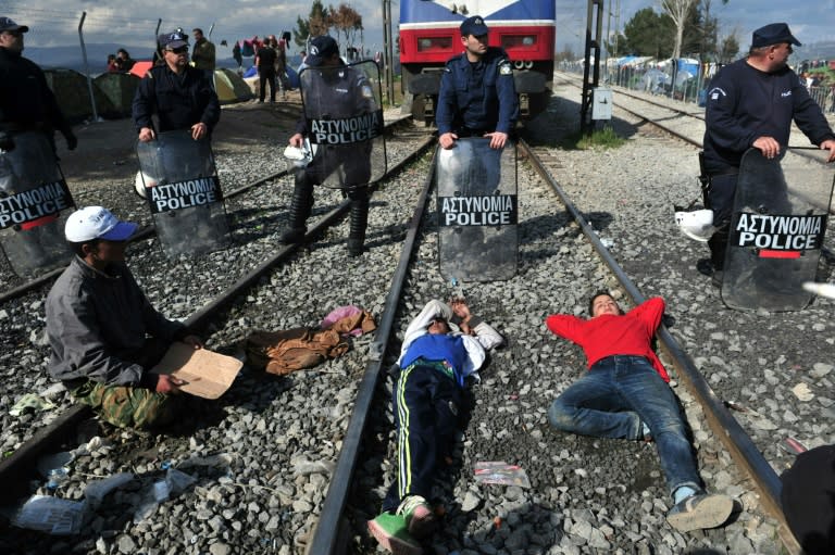 People sit and lie on train tracks in front of Greek policemen during a protest of migrants and refugees to call for the opening of the borders, at the Greek-Macedonian border near the Greek village of Idomeni on March 3, 2016