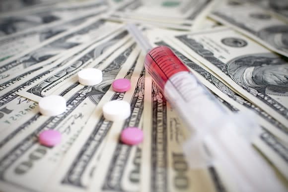 Pills and a syringe on a pile of hundred-dollar bills.