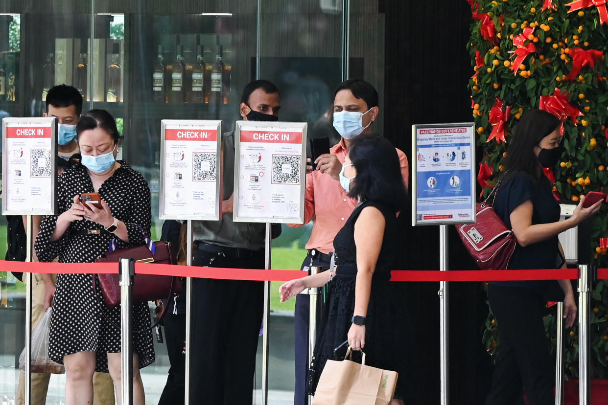 People scan QR codes using the Trace Together contact tracing app on their smartphones before entering a building at the Raffles Place financial business district in Singapore on February 14, 2022. (Photo by Roslan RAHMAN / AFP) (Photo by ROSLAN RAHMAN/AFP via Getty Images)