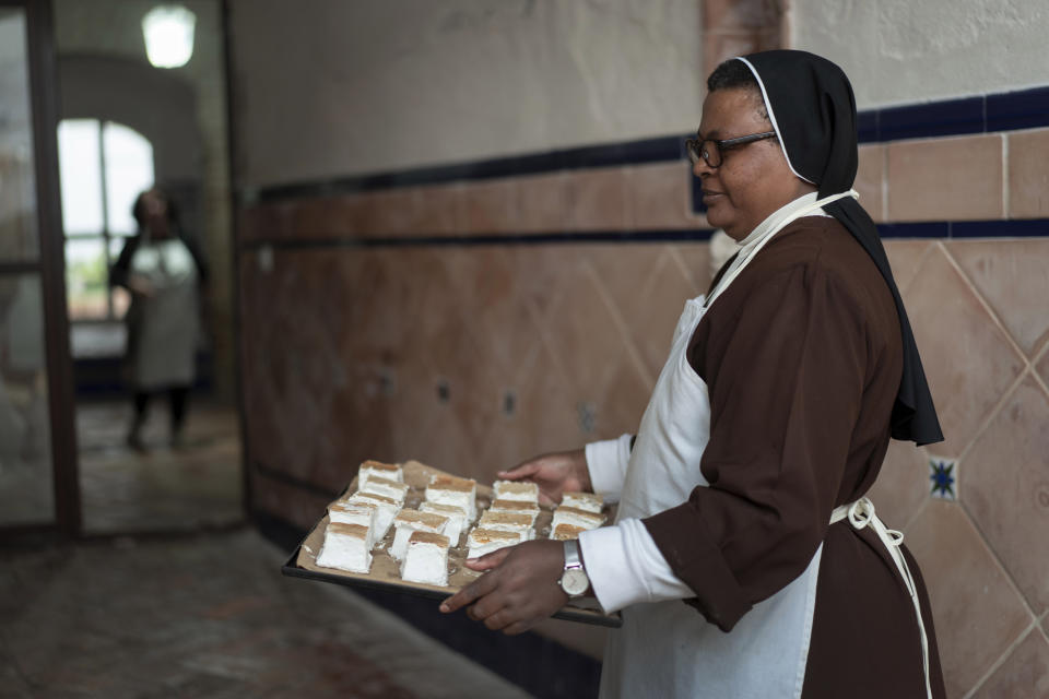 Nun Veronicah Nzula, 47, from Kenya, carries cakes after taking them out of the oven at the Clarisas convent in Carmona, Spain, on Thursday, Nov. 30, 2023. It's the fortnight before Christmas and all through the world's Catholic convents, nuns and monks are extra busy preparing the traditional delicacies they sell to a loyal fan base even in rapidly secularizing countries. (AP Photo/Laura Leon)