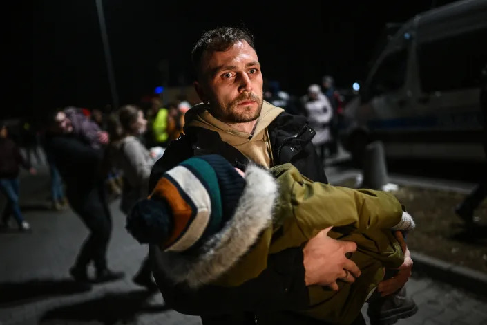 PRZEMYSL, POLAND - FEBRUARY 25: A man holds a sleeping baby after arriving by bus to a supermarket parking lot from the Polish-Ukrainian border crossing on February 25, 2022 in Przemysl, Poland.