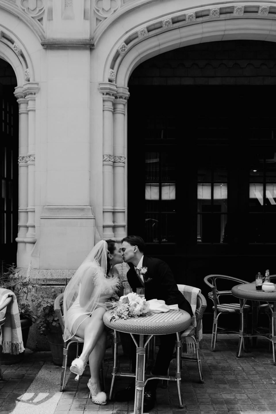 A black and white photo of a bride and groom kissing at an outdoor table on their wedding table.