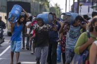 FILE - People carry gas cylinders after they bought it at a distribution center, in Colombo, Sri Lanka, July 12, 2022. Most Asian countries are prioritizing keeping the country running, no matter the energy source. Enormous debts prevent it from buying energy on credit, forcing it to ration fuel for key sectors with shortages anticipated for the next year. (AP Photo/Rafiq Maqbool, File)