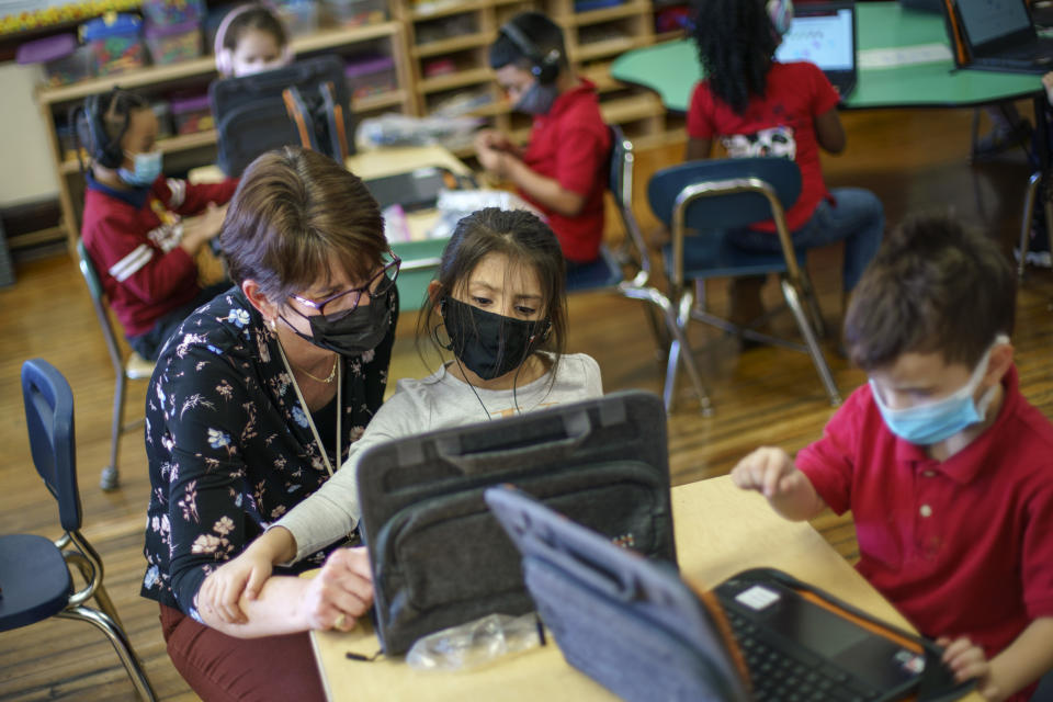 FILE - Kindergarten teacher Karen Drolet, left, works with a student at Raices Dual Language Academy, a public school in Central Falls, R.I., Feb. 9, 2022. As a new school year approaches, COVID-19 infections are again on the rise, fueled by highly transmissible variants, filling families with dread. They fear the return of a pandemic scourge: outbreaks that sideline large numbers of teachers, close school buildings and force students back into remote learning. (AP Photo/David Goldman, File)