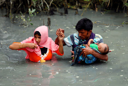 Rohingya refugees carry their child as they walk through water after crossing border by boat through the Naf River in Teknaf, Bangladesh, September 7, 2017. REUTERS/Mohammad Ponir Hossain