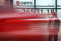 A man wearing a protective face mask to help curb the spread of the coronavirus stands near an electronic stock board showing Japan's Nikkei 225 index at a securities firm as a car passing by Friday, Nov. 27, 2020, in Tokyo. Asian stock markets declined Friday as questions about the effectiveness of one possible coronavirus vaccine weighed on investor optimism. (AP Photo/Eugene Hoshiko)