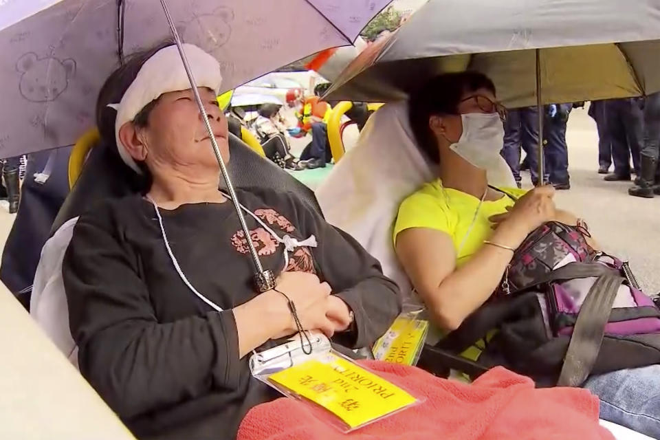 In this image taken from a video footage run by TVB, women wait to be treated after they were injured in the aftermath of an accident where four passenger buses and a truck collided near a Hong Kong road tunnel on Friday, March 24, 2023. Dozens were injured, including children. Most of the injuries were minor. (AP Photo/TVB via AP)