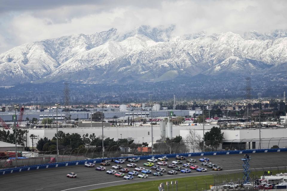 With snow-covered mountains in the distance, cars drive in a five-line formation to acknowledge the fans before a NASCAR Cup Series auto race at Auto Club Speedway in Fontana, Calif., Sunday, Feb. 26, 2023. The track hosts its finalNASCAR Cuprace Sunday. (AP Photo/Jae C. Hong)