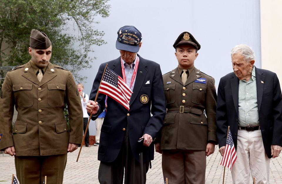 Veteran WWII pilot Maj. John "Lucky" Luckadoo holds a flag as he's joined by fellow Veteran TSgt. Gordon Fenwick and a pair of costumed reenactors,on Friday. May 26, 2023 during the Flags for the Fallen opening ceremony at the National Museum of the Mighty 8th Air Force.