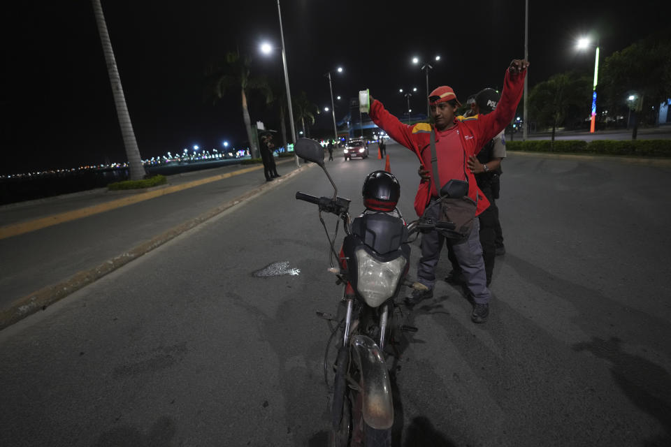 Police frisk a motorcycle driver for weapons during the start of a curfew decreed by Ecuador´s President Guillermo Lasso to try to reduce the ongoing wave of violence in Manta, Ecuador, Monday, July 24, 2023. (AP Photo/Dolores Ochoa)