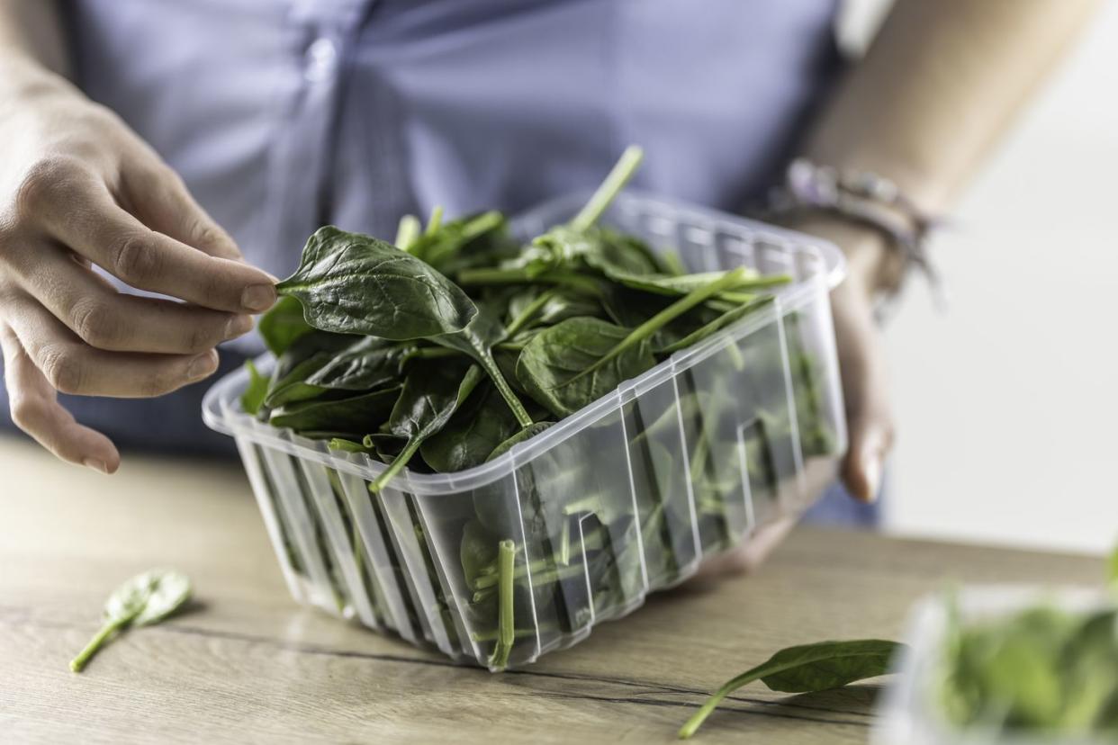 female hands hold a plastic package with baby spinach in her kitchen