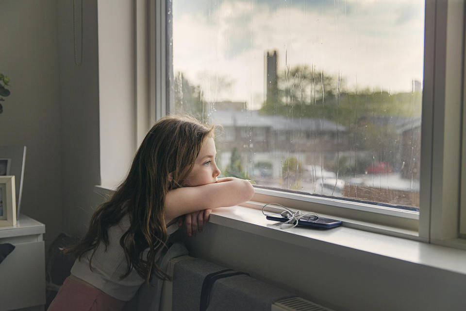 Young girl looking out of window on a rainy day (Getty Images)