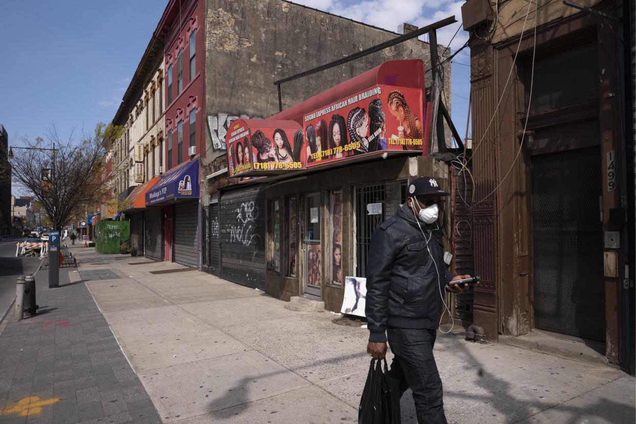 A man wearing a mask walks past Sogho Express African Hair Braiding salon, which is closed due to the coronavirus pandemic, Tuesday, April 7, 2020 in the Bedford Stuyvesant neighborhood of New York. 