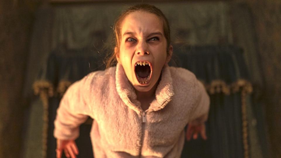 A child vampire bares her sharp teeth in Abigail