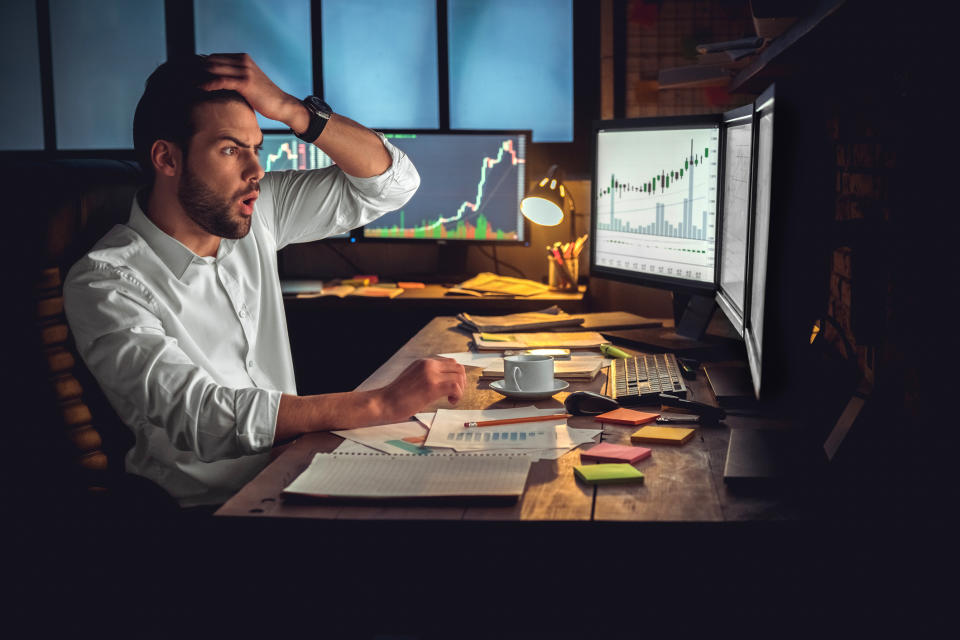 A worried person looks at stock charts on a computer screen.