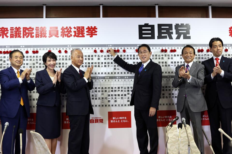 Japan's Prime Minister and ruling Liberal Democratic Party leader Fumio Kishida, third from right, poses with key party members as he puts rosettes by successful general election candidates' names on a board at the party headquarters in Tokyo, Sunday, Oct. 31, 2021. Japanese Prime Minister Fumio Kishida’s governing coalition is expected to keep a majority in a parliamentary election Sunday but will lose some seats in a setback for his weeks-old government grappling with a coronavirus-battered economy and regional security challenges, according to exit polls. (Behrouz Mehri, Pool via AP)