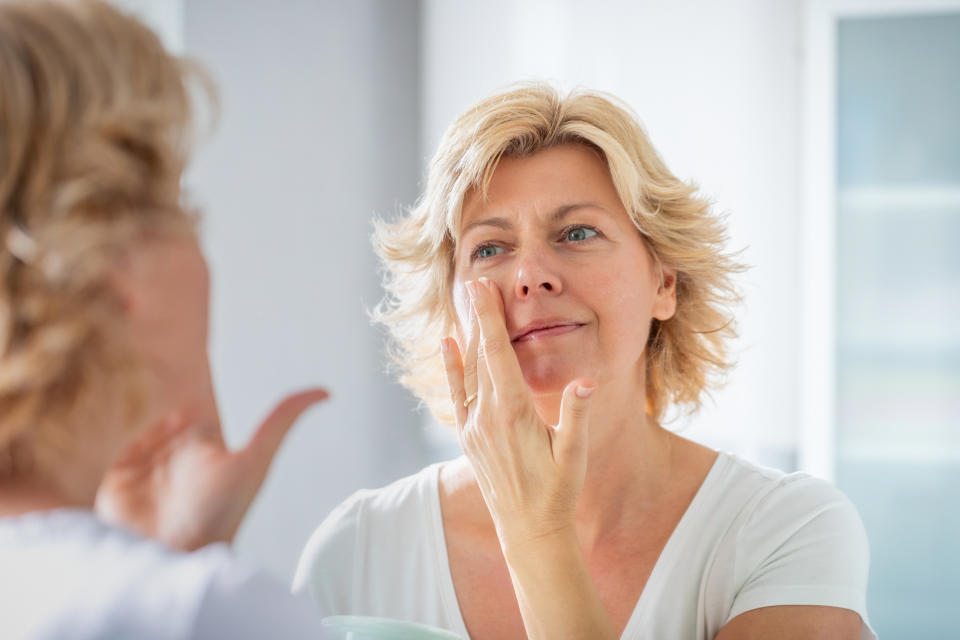 Mid adult woman standing in front of the bathroom mirror and spreading a layer of facial cream on her cheeks