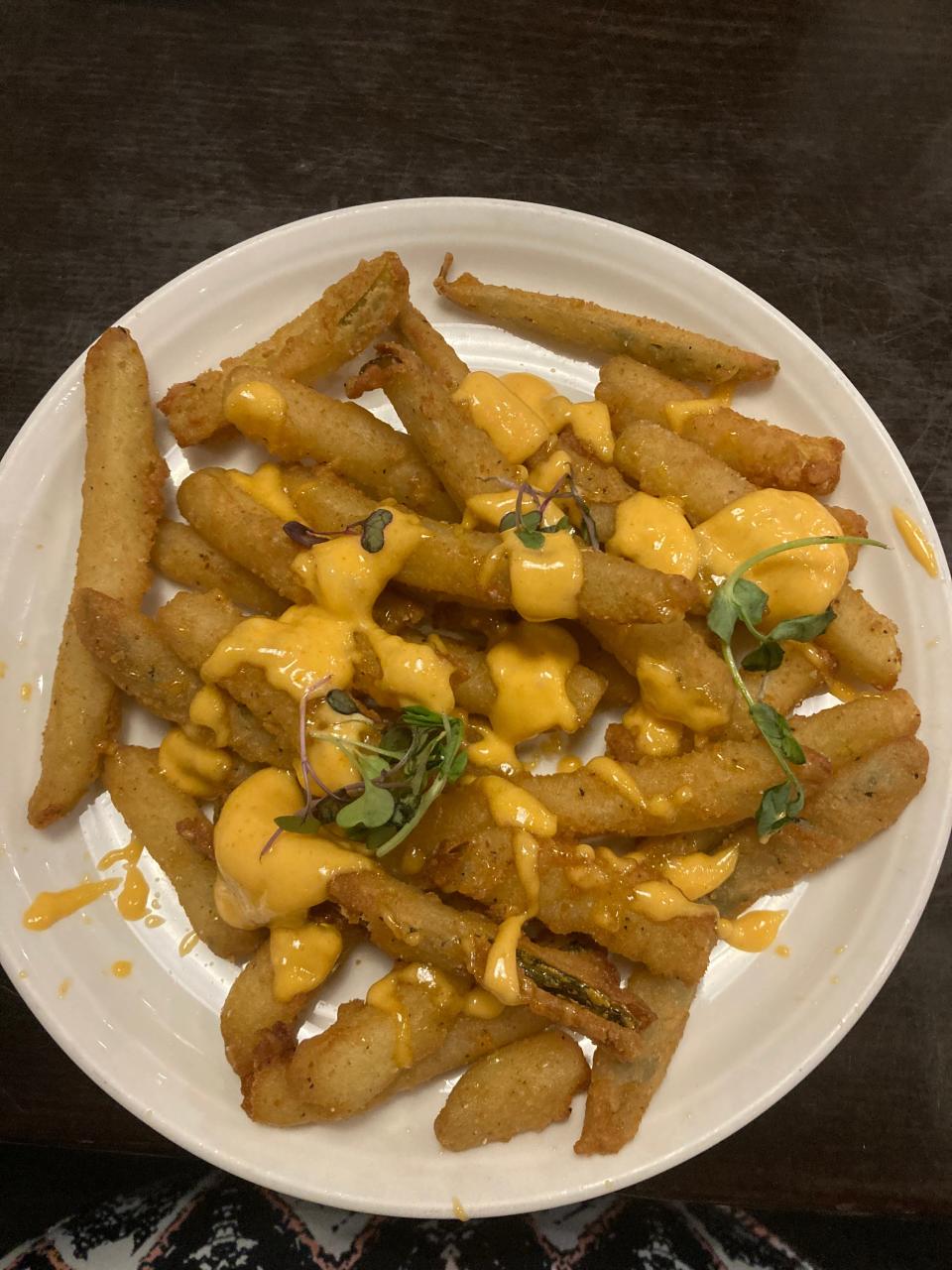 A plate of breaded pickle fries topped with a spicy aioli and microgreens.