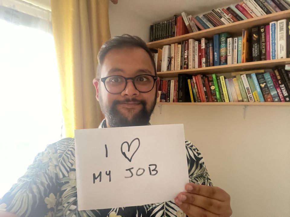 Tufayel Ahmed holding a sign that says "I [heart] my job."