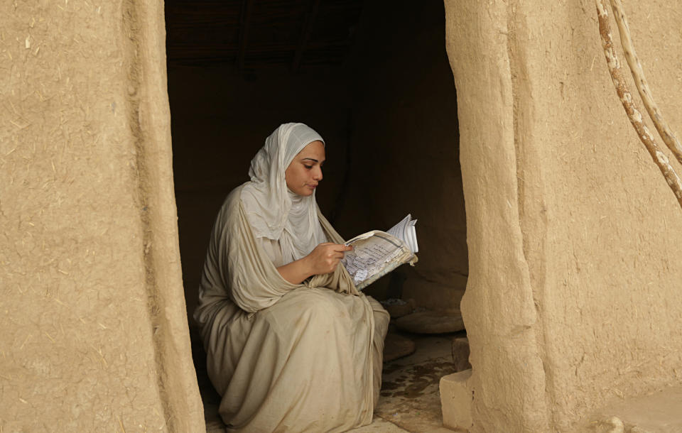 In this Sunday, Oct. 14, 2018 photo, a follower of the obscure and ancient Mandaean faith reads from a religious book in the doorway of a mud building along a strip of embankment on the Tigris River reserved for them, in Baghdad, Iraq. Mandaeism follows the teachings of John the Baptist, a saint in both the Christian and Islamic traditions, and its rites revolve around water. (AP Photo/Hadi Mizban)