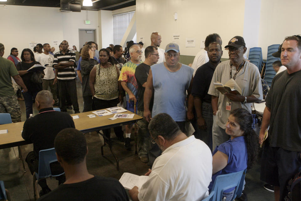 FILE - In this July 30, 2009, file photo, people gather at the Midnight Mission on Skid Row in Los Angeles. Starting this week, census takers are grabbing reflective vests, face masks, bug spray and flashlights and heading out at night in groups of four to track down one of the hardest populations to count in the 2020 census — the homeless. (AP Photo/Nick Ut, File)