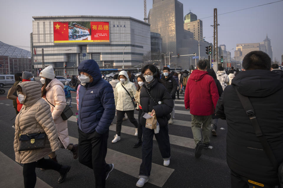 Commuters wearing face masks walk across an intersection near an electronic billboard for China's armed forces during the morning rush hour in Beijing, Friday, Feb. 10, 2023. (AP Photo/Mark Schiefelbein)