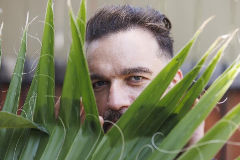 Los Angeles, CA - August 09: Francesco Cura peaks through a palm at a community garden he maintains in his neighborhood at the intersection of Normandie and Harold on Friday, Aug. 9, 2024 in Los Angeles, CA. (Carlin Stiehl / For the Times)