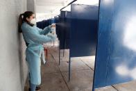 Una mujer con una mascarilla protectora y un traje desinfecta una cabina de votación durante un referéndum sobre una nueva constitución en Santiago de Chile.