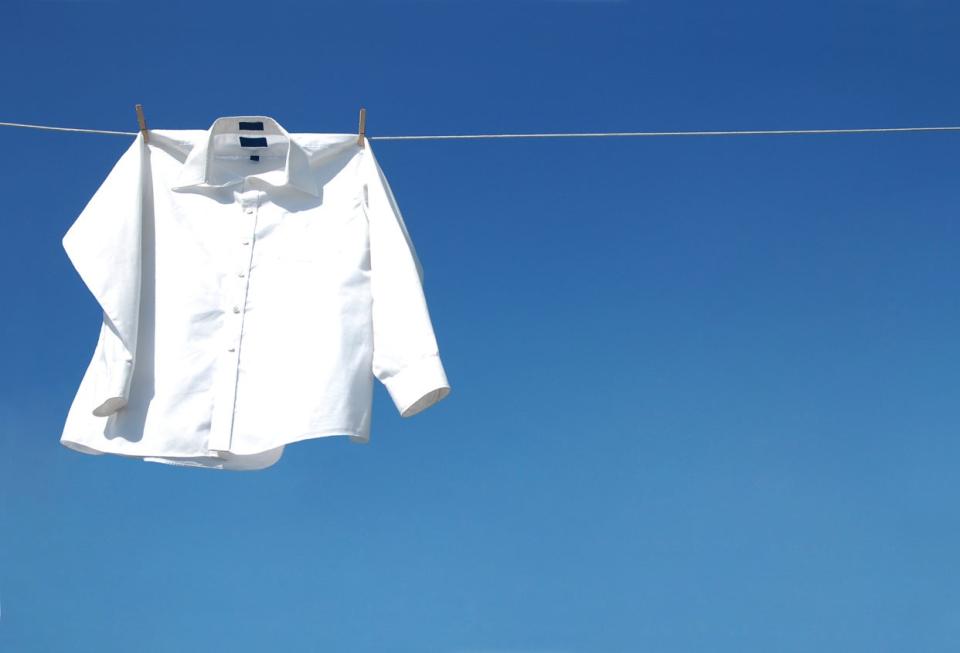 a crisp white blouse hanging on clothesline in front of bright blue sky