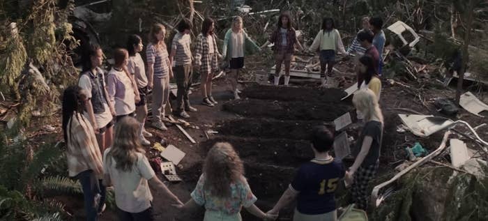 A scene from 'Yellowjackets' with survivors of the plane crash holding hands in a circle around the graves of their teammates