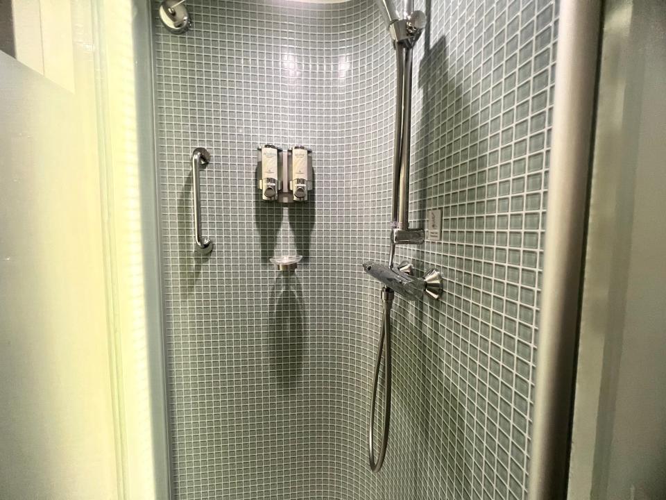 Norwegian Getaway studio stateroom shower interior, blue towels with shower head and soaps on wall