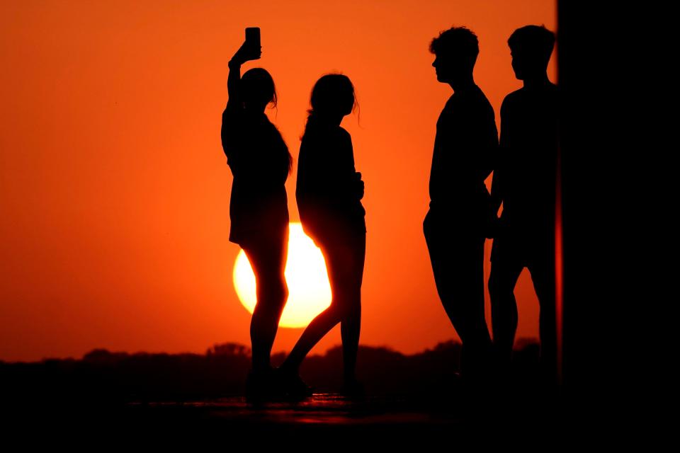 People in Kansas City, MO on Wednesday against a sunset turned vibrant orange by smoke from the New Mexico fires drifting east (AP)