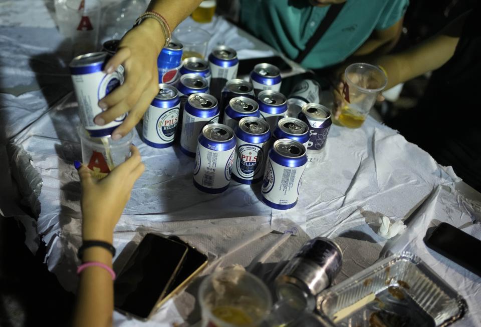 People drink beers during a festivity, known as Panigiri, in Aski village about 115 kilometers (72 miles) north of Athens, Greece, early Sunday, Aug. 14, 2022. The Dormition of the Virgin Mary (or Mother of God as the Greeks usually refer to her) is celebrated on Aug. 15. The religious event is coupled with midsummer festivities, known as Panigiria, that often last more than a day with music, culinary feasts and, in many cases, flea markets. (AP Photo/Thanassis Stavrakis)