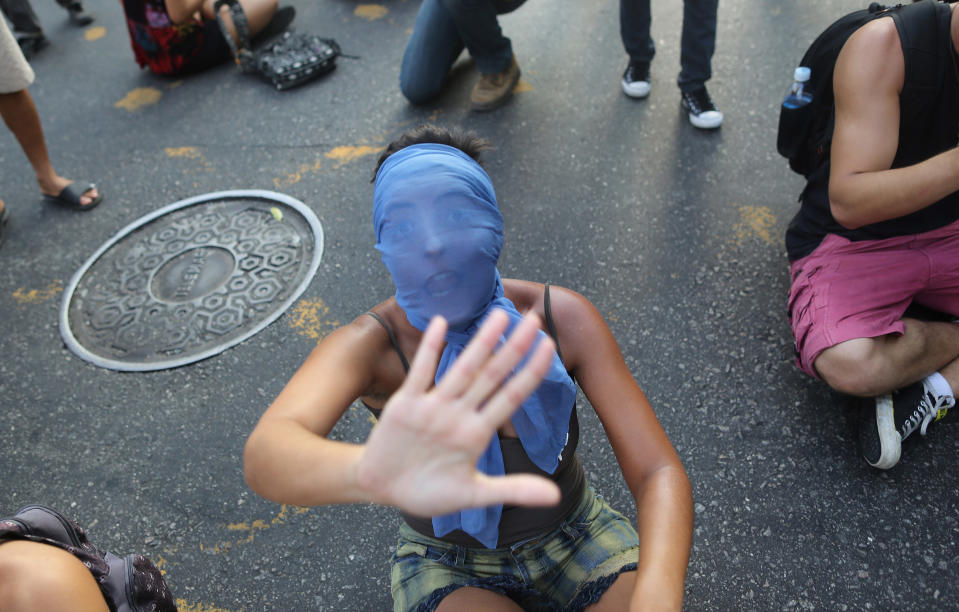 A masked girl shouts while sitting on the street, in protest against the increase on bus fares in Rio de Janeiro, Brazil, Monday, Feb. 10, 2014. Anti-government protests erupted across Brazil last June, hitting their peak as 1 million Brazilians took to streets on a single night, calling for better schools and health care and questioning the billions spent to host this year's World Cup and the 2016 Olympics. The protests have since diminished in size, but remain violent. (AP Photo/Leo Correa)