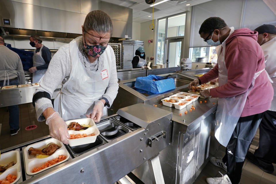 Volunteers Sheeran Howard, left, and Ibrahim Bahrr, right, package meals at Community Servings, which prepares and delivers scratch-made, medically tailored meals to individuals & families living with critical & chronic illnesses, Tuesday, Jan. 12, 2021, in the Jamaica Plain neighborhood of Boston. Food is a growing focus for insurers as they look to improve the health of the people they cover and cut costs. Insurers first started covering Community Servings meals about five years ago, and CEO David Waters says they now cover close to 40%. (AP Photo/Charles Krupa)