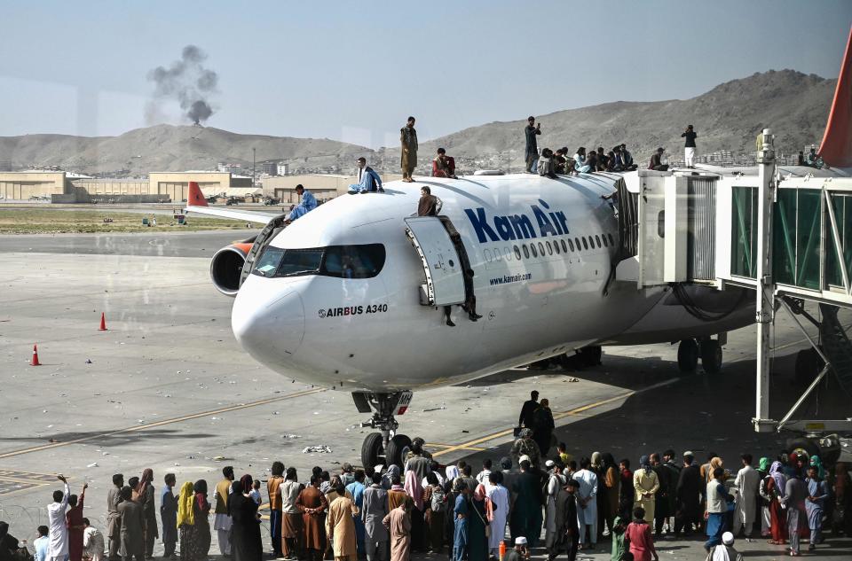 Afghan people climb atop a plane as they wait at the Kabul airport in Kabul on Aug. 16, 2021, as thousands of people mobbed the city's airport trying to flee the group's feared hardline brand of Islamist rule.