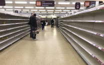 FILE - In this Thursday, March 19, 2020 file photo, people stand in an aisle of empty shelves in a supermarket in London, amid panic-buying due to the coronavirus outbreak. A pandemic forcing everyone to stay home could be the perfect moment for online grocery services. In practice, they've been struggling to keep up with a surge in orders, highlighting their limited ability to respond to an unprecedented onslaught of demand. After panic buying left store shelves stripped of staples like pasta, canned goods and toilet paper, many shoppers quickly found online grocery delivery slots almost impossible to come by, too. (AP Photo/Kirsty Wigglesworth, File)