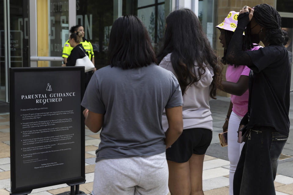 A security guard stands by as teens read a sign explaining the Mall in Columbia's "Parental Guidance Required" program, Friday, May 12, 2023, in Columbia, Md. The program requires that all visitors under 18 be accompanied by an adult who is at least 21-years-old after 4 p.m. on Fridays and Saturdays. (AP Photo/Julia Nikhinson)