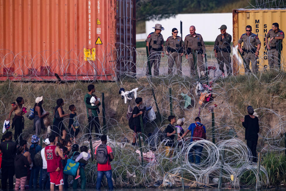 Texas Department of Public Safety troopers observe migrants from behind concertina wire after the migrants crossed the Rio Grande into Eagle Pass in July.