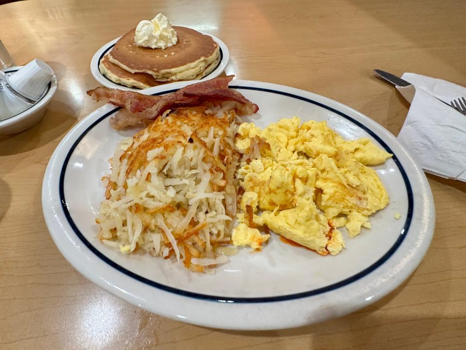 One large plate with eggs, hash browns, and bacon and a smaller plate with two pancakes on wood table at IHOP