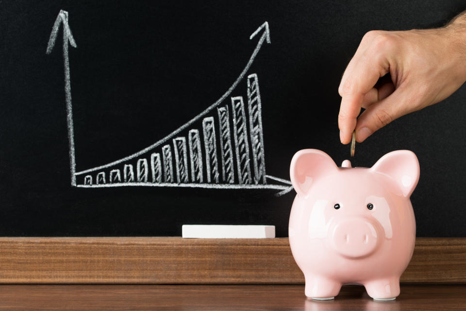 Man inserting coin into piggy bank in front of blackboard with bar graph indicating upward growth