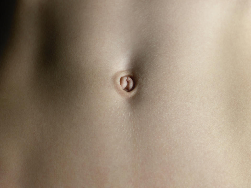 Close-up of a person’s bare stomach and navel, showing a clean and smooth skin surface