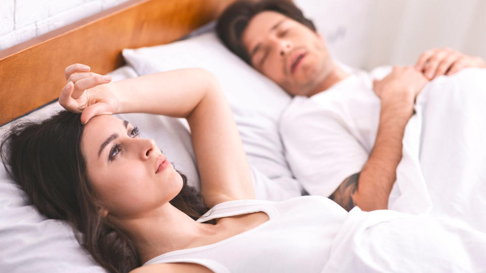 woman lying awake in bed besides her sleeping male partner