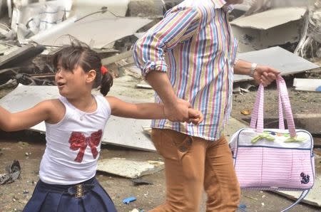 A man holds the hand of a girl as they rush out after rebels bombarded government-held areas of Aleppo, Syria, in this handout picture provided by SANA on May 3, 2016. SANA/Handout via REUTERS